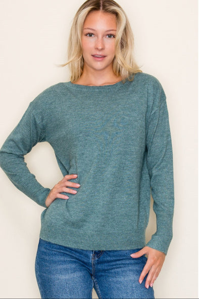 Woman wearing a teal sweater and blue jeans against a plain background