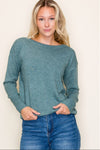 Woman wearing a teal sweater and blue jeans against a plain background